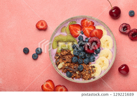 Delicious acai bowl with fresh fruits and granola in white ceramic bowl on pink table top view, healthy breakfast or snack 129221689