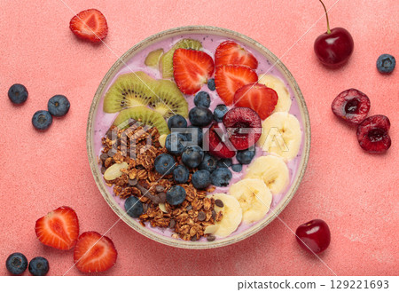 Delicious acai bowl with fresh fruits and granola in white ceramic bowl on pink table top view, healthy breakfast or snack 129221693