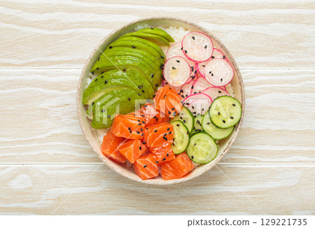 Salmon poke bowl with avocado, radish, cucumber and rice on white wooden background top view Salmon poke bowl with avocado, radish, cucumber and rice on white wooden background top view 129221735