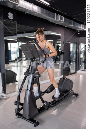 A woman is actively exercising on an elliptical machine at a modern gym facility A woman is actively exercising on an elliptical machine at a modern gym facility 129221825