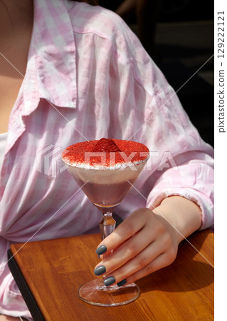 Woman holding a fancy cocktail with whipped cream and red topping Woman holding a fancy cocktail with whipped cream and red topping 129222121