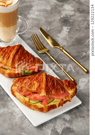 Delicious croissant sandwiches with salmon and cucumber filling accompanied by latte coffee Delicious croissant sandwiches with salmon and cucumber filling accompanied by latte coffee 129222134