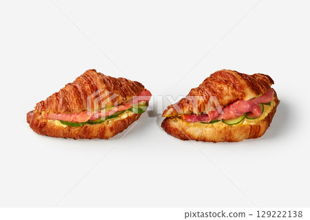 Two delicious croissant sandwiches with salmon, cucumber and cheese filling on white background Two delicious croissant sandwiches with salmon, cucumber and cheese filling on white background 129222138