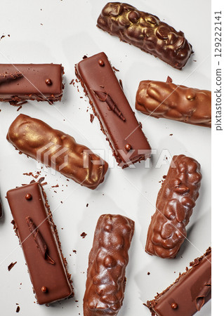Delicious chocolate bars covered in nuts and chocolate shavings resting on white background 129222141