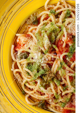 Delicious italian spaghetti with pesto, tomato sauce and capers being served on yellow plate 129222208