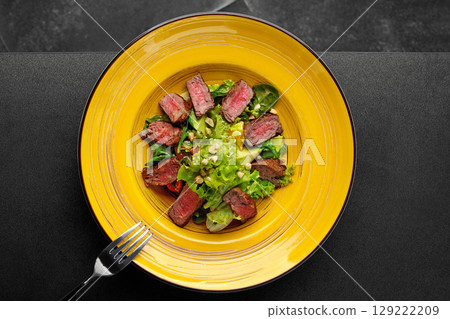 Warm salad with grilled medium-rare steak, lettuce, avocado, and nuts served on yellow plate Warm salad with grilled medium-rare steak, lettuce, avocado, and nuts served on yellow plate 129222209