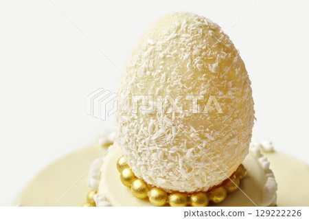 Delicious white chocolate easter egg resting on a cake decorated with gold and white chocolate 129222226