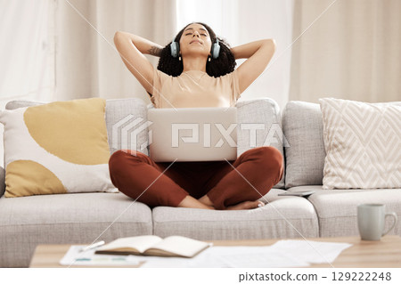 Black woman, headphones and laptop to relax, on couch for wellness and meditation in living room. Young female, girl and earphones for podcast, rest and on break for health, calm and peaceful on sofa 129222248
