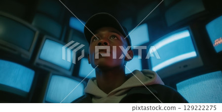Young Man Standing in Front of Wall of Glowing Blue TV Screens 129222275
