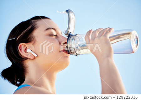 Drinking water, fitness and music with a sports woman hydrating during a run on a blue sky background outdoor. Wellness, health and exercise with a female runner or athlete taking a drink to hydrate Drinking water, fitness and music with a sports woman hydrating during a run on a blue sky background outdoor. Wellness, health and exercise with a female runner or athlete taking a drink to hydrate 129222316