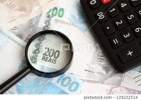 Brazilian reais banknotes and calculator with magnifying glass. Brazil real money, calc with loupe Brazilian reais banknotes and calculator with magnifying glass. Brazil real money, calc with loupe 129222514