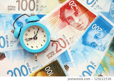 Israel New Shekels banknotes and alarm clock. The current Israel money bills and clock lies on table Israel New Shekels banknotes and alarm clock. The current Israel money bills and clock lies on table 129222536
