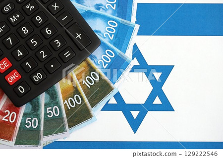 Israel New Shekels banknotes and calculator on flag. The Israel money bills and calc lies on flag Israel New Shekels banknotes and calculator on flag. The Israel money bills and calc lies on flag 129222546