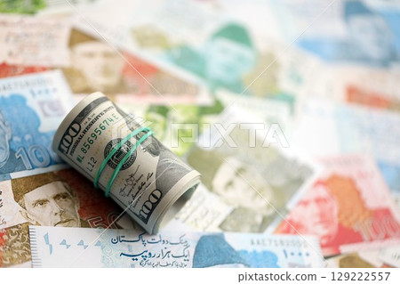 Roll of US dollar bills lies on big amount of Pakistan rupees banknotes close up Roll of US dollar bills lies on big amount of Pakistan rupees banknotes close up 129222557