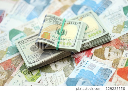 Bunch of US dollar bills lies on big amount of Pakistan rupees banknotes close up Bunch of US dollar bills lies on big amount of Pakistan rupees banknotes close up 129222558