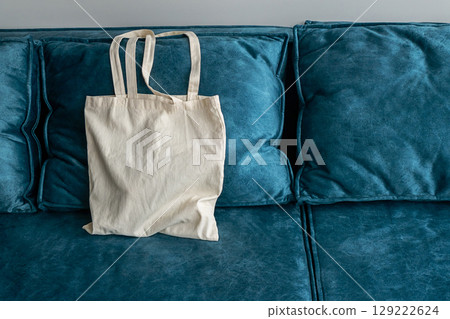 White canvas eco friendly tote bag on a plush teal sofa. White canvas eco friendly tote bag on a plush teal sofa. 129222624
