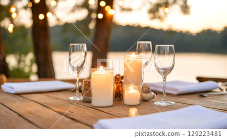 Candlelit dinner table with wine glasses beside a serene lakeside view 129223481