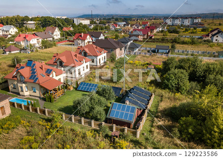Aerial view of a new autonomous house with solar panels, water heating radiators on the roof, wind powered turbine and green yard with blue swimming pool. 129223586