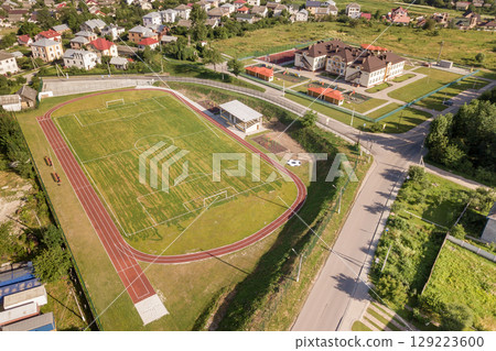 Aerial view of a football field on a stadium covered with green grass in rural town area. Aerial view of a football field on a stadium covered with green grass in rural town area. 129223600