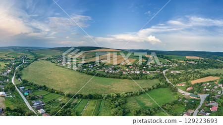 Aerial landscape view of village houses and distant green cultivated agricultural fields with growing crops on bright summer day 129223693