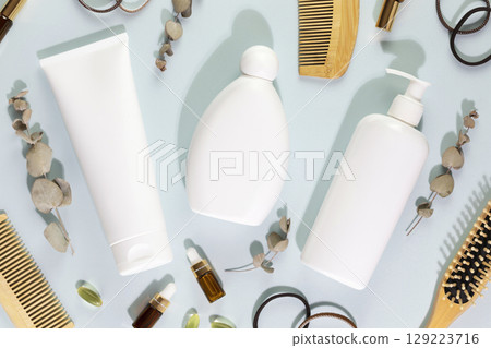 Hair cosmetics. Hair care card with shampoo and conditioner bottles with combs, mask for hair, oil, and eucalyptus on a blue background. Mock up of natural beauty products for hair. Soft image style 129223716