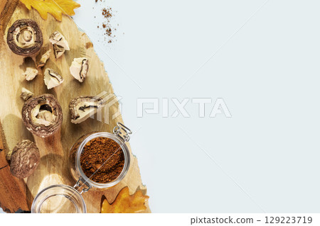 Superfood. Pieces of dry mushrooms with chaga powder in a glass jar on a wooden podium with autumn leaves on a blue background with copy space. Mushroom Chaga Coffee 129223719