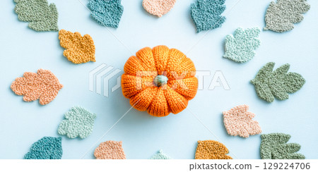 Knitted Pumpkin Surrounded By Soft Colorful Leaves On Light Blue Background. Concept Of Cozy Autumn Decor, Handmade Crafts, DIY, Seasonal Aesthetics, And Fall-Themed Visuals For Home Brands 129224706