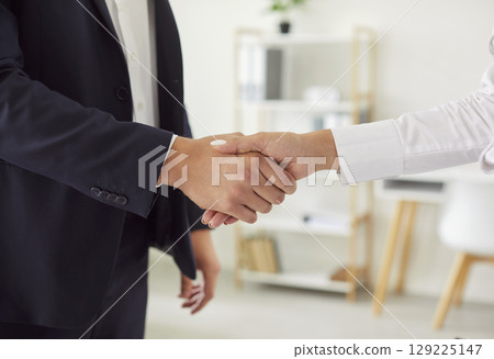 Close up of business man shaking hands with his female partner standing in office 129225147