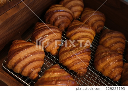 Croissants cooling rack Croissants Stacked on Wire Rack Cooling Rack. Natural light illuminates the golden brown. conveying the aroma and appetising appearance of the baked goods 129225193