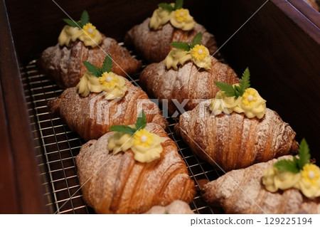 Croissants mango freshly baked croissants and sweet bread on a plate with vibrant mango cubes. Sunlight creates a warm ambiance on the rustic table, enhancing the cozy breakfast setting. 129225194