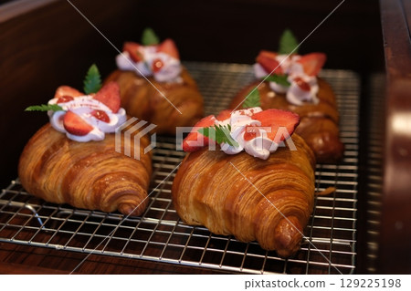 Crispy sweet red croissant with pistachio, raspberry and strawberry on a dark concrete background 129225198
