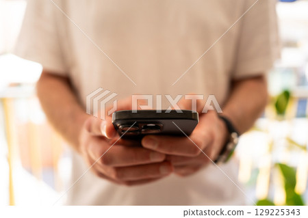 Close-up of man in white t-shirt typing message on mobile phone Close-up of man in white t-shirt typing message on mobile phone 129225343
