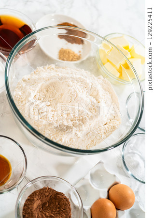 Top view of ingredients for Chocolate Ginger Sugar Cookie Dough, including flour, butter, eggs, brown sugar, maple syrup, cocoa, and spices, all arranged on a marble surface. 129225411
