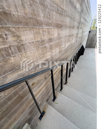A set of wide exterior concrete stairs bordered by smooth concrete walls and a black metal handrail. The stairway connects the elevated clubhouse entrance to lower walkways. A set of wide exterior concrete stairs bordered by smooth concrete walls and a black metal handrail. The stairway connects the elevated clubhouse entrance to lower walkways. 129225412