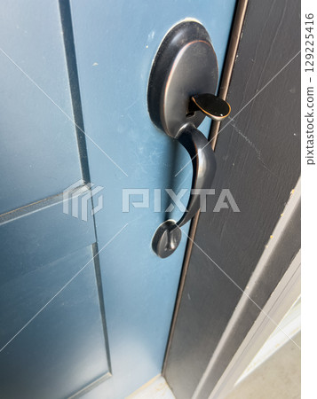 A modern matte black door handle with a curved design is mounted on a navy-colored front door. The close-up view highlights the clean finish and sturdy form. A modern matte black door handle with a curved design is mounted on a navy-colored front door. The close-up view highlights the clean finish and sturdy form. 129225416