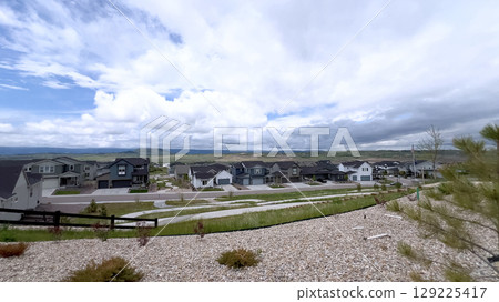 Several modern homes are built along a sloped street in a residential community. Cloudy skies and open land dominate the background. Several modern homes are built along a sloped street in a residential community. Cloudy skies and open land dominate the background. 129225417