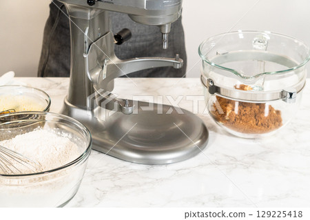 Eye-level view of a stand mixer with a glass bowl, blending the ingredients for Classic Gingerbread Cookie Dough. Visible layers include the dark molasses mixture and brown sugar, ready to be combined Eye-level view of a stand mixer with a glass bowl, blending the ingredients for Classic Gingerbread Cookie Dough. Visible layers include the dark molasses mixture and brown sugar, ready to be combined 129225418
