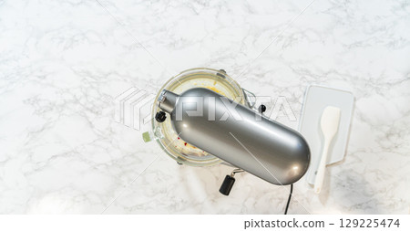 A close-up of dough for lemon spritz cookies in a stand mixer, ready for piping and shaping into delicate cookie shapes. A spatula is visible for scraping the bowl. 129225474