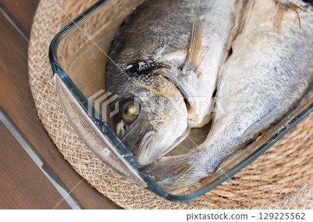 Freshly prepared Dorado fish displayed in a transparent glass baking dish 129225562