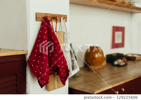 A kitchen scene featuring a wooden cabinet with a checkered orange and white dish towel hanging from a hook. The floor is made of wooden planks, and the background suggests a bright kitchen. 129225606