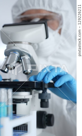 Scientific researcher wearing protective gear adjusting microscope, analyzing lab samples with precision in sterile research environment. Medicine, healthcare and science concept Scientific researcher wearing protective gear adjusting microscope, analyzing lab samples with precision in sterile research environment. Medicine, healthcare and science concept 129226211
