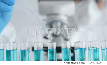 Close up of scientific researcher wearing protective gear, carefully pipetting liquid into test tubes while conducting medical research experiment in laboratory. Medicine, healthcare and science Close up of scientific researcher wearing protective gear, carefully pipetting liquid into test tubes while conducting medical research experiment in laboratory. Medicine, healthcare and science 129226213