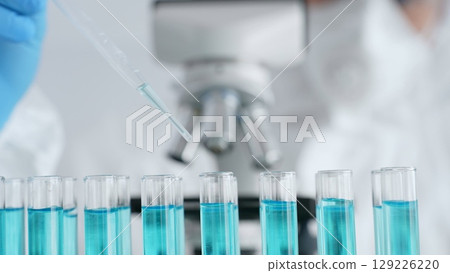 Close up of scientific researcher wearing protective gear, carefully pipetting liquid into test tubes while conducting medical research experiment in laboratory. Medicine, healthcare and science 129226220