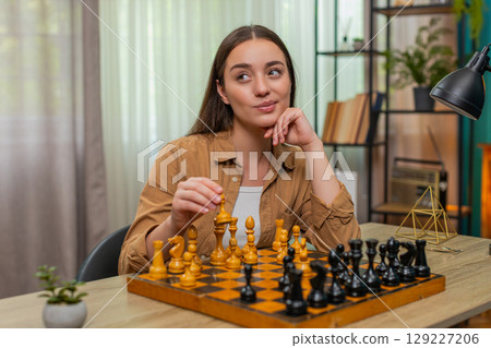 Woman playing chess alone thinking deeply moving pieces slowly planning careful strategic steps Woman playing chess alone thinking deeply moving pieces slowly planning careful strategic steps 129227206