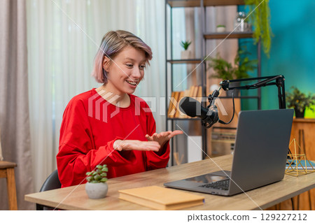 Young confident woman recording video interview at laptop speaking seriously in studio microphone 129227212