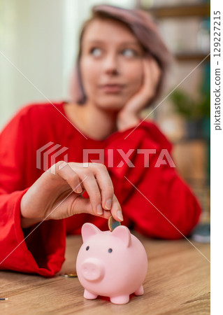 Young woman happily putting coins into piggy bank smiling expressing financial discipline budgeting 129227215