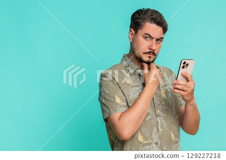 Adult man looking seriously at smartphone reading business news or analytics with focused expression Adult man looking seriously at smartphone reading business news or analytics with focused expression 129227218