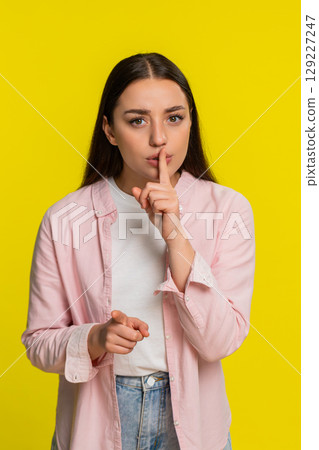 Woman placing finger on lips showing silence gesture asking for quiet serious thoughtful expression 129227247