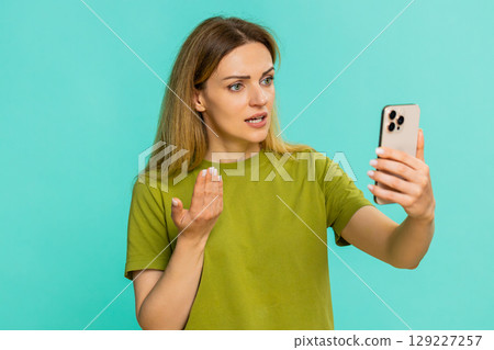 Woman holding smartphone having tense speakerphone conversation with sad emotional facial expression Woman holding smartphone having tense speakerphone conversation with sad emotional facial expression 129227257