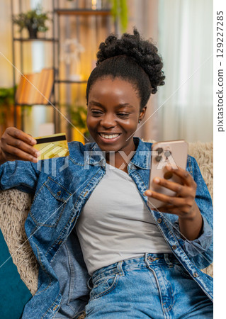 African American young woman shopping online on smartphone with credit card, smiling after purchase African American young woman shopping online on smartphone with credit card, smiling after purchase 129227285